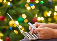 Holiday shopping using laptop computer, photographed against christmas tree lights